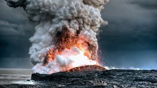 A volcano erupts in Hawaii near the water.