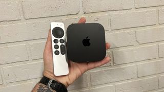 An Apple TV 4K and remote in hand