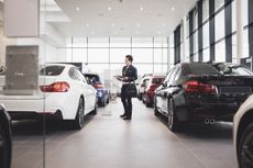 Woman holding brochure and looking at cars in a dealership or showroom
