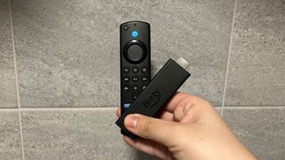 The Amazon Fire TV Stick 4K Max with remote control held in front of a tiled wall.