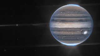 jupiter appears as bands of brown and beige with two bright blue glowing regions of auroras at either pole of the planet.