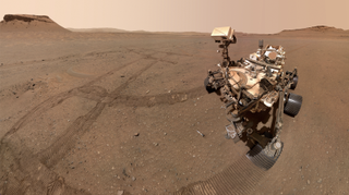 a four-wheeled robot with a head-like box atop a neck-like appendage looks down at a silver tube lying on the dusty reddish-orange surface of Mars