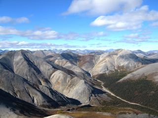 Plate tectonics is the means through which mountains are formed. Image shows rippled gray mountains, mostly treeless, beneath a cloud-studded blue sky. The Baird Mountains in Alaska’s Kobuk Valley National Park formed when two tectonic plates along a convergent boundary collided, causing solid rock to buckle and fold.