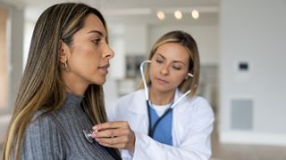 Doctor placing a stethoscope on a female patient's chest over the patient's sweater