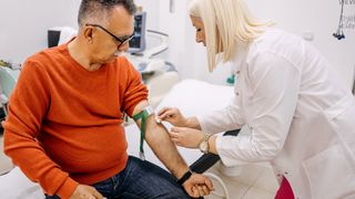 Nurse wiping an older male patient's arm with a cotton swab as she preps for a blood draw