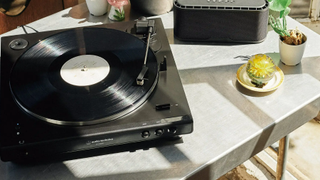 Audio Technica AT-LP60XBT on a table with a bluetooth speaker and two small potted plants in the sun