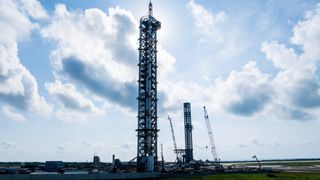 two large metallic launch towers stand beneath a cloudy blue sky