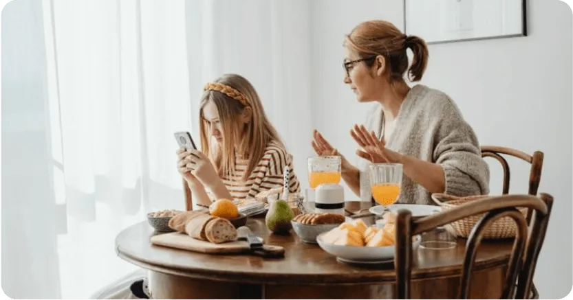 Parent and child at breakfast table, child is holding a phone up to her face