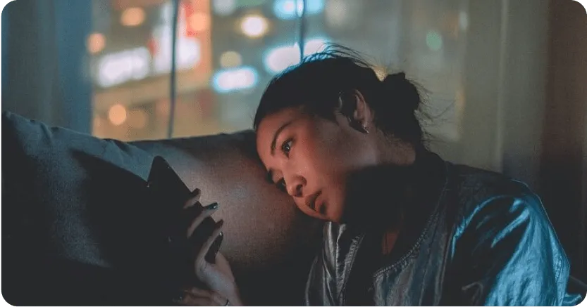 Teenage girl in dark room on a couch holding a phone up to her face