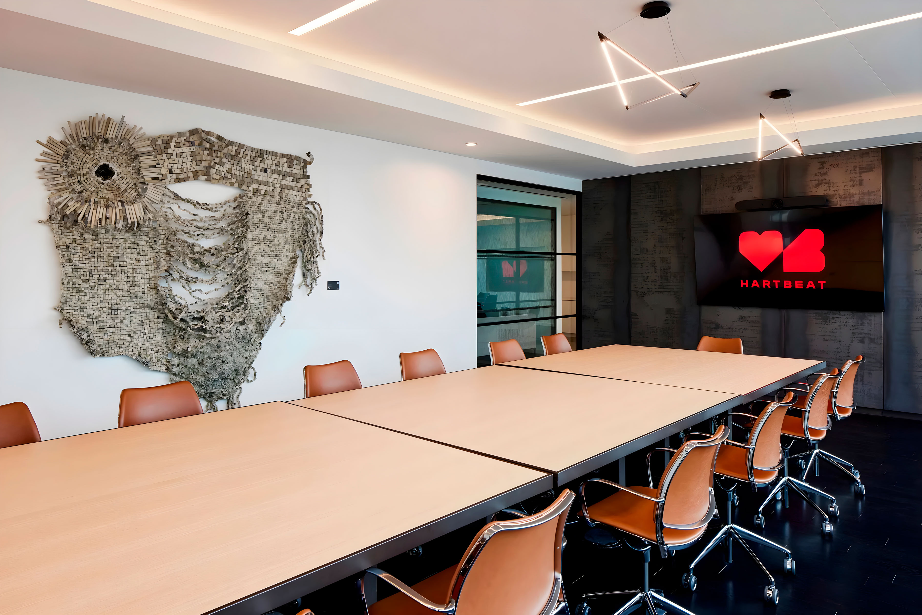 A large office table with chairs, a large artwork hanging on the wall, and a television in the background