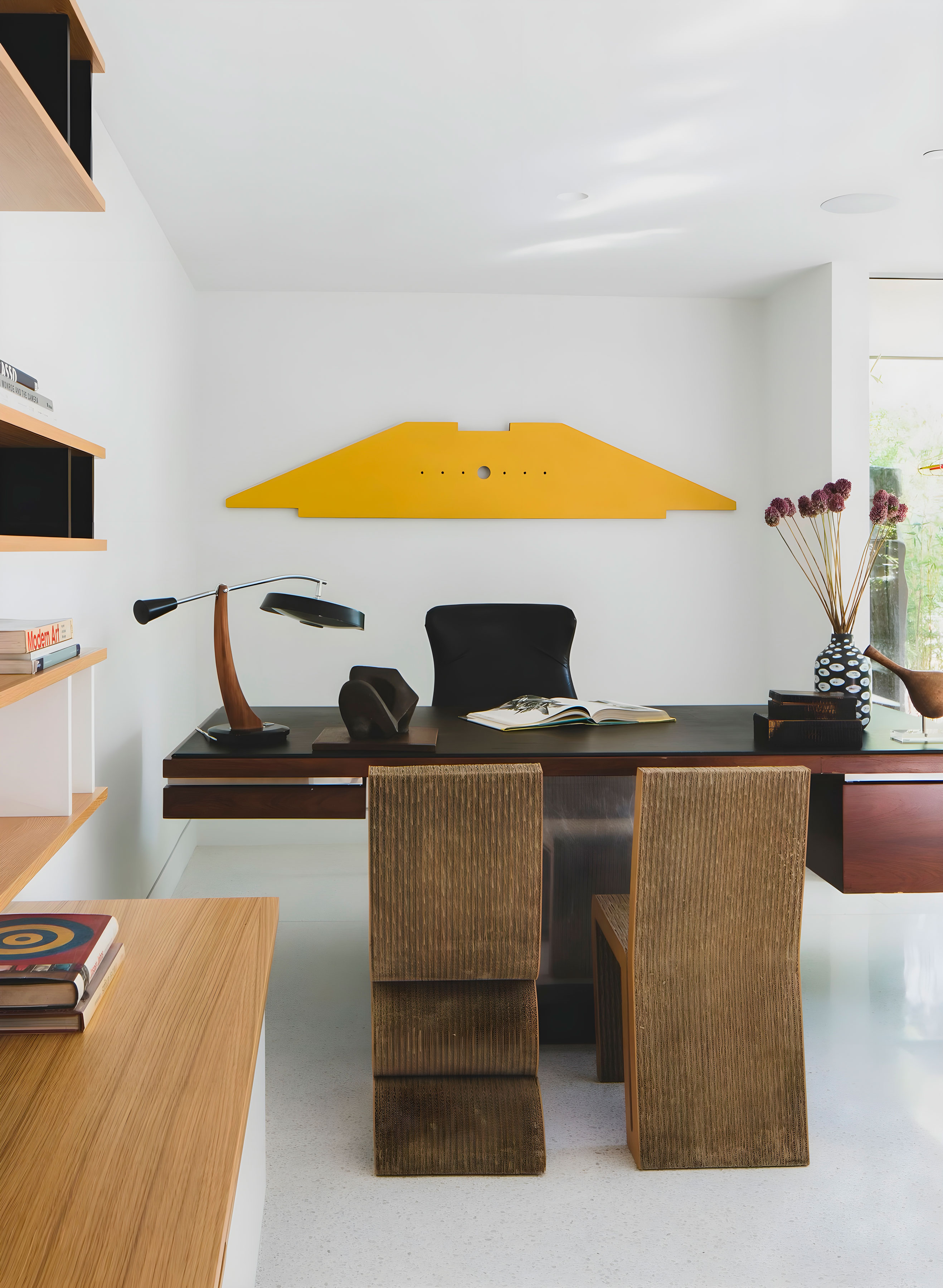 A desk with a chair, and an artwork hanging above it 