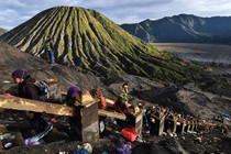 People climb a steep staircase up the side of a mountain, with a volcano in the background.