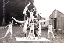 A black-and-white photo shows a team of 11 gymnasts posing in variously difficult stances, forming a symmetric scene.