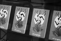 A black and white image of four 'Maus' books on a shelf. The cover depicts two mice huddled together under a swastika that bears the image of a cat drawn to look like Hitler