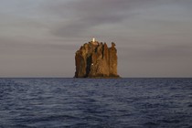 A small isolated island with tall sheer cliffs, topped by a lighthouse