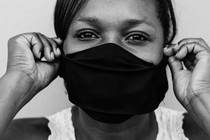 Black-and-white close-up of a woman putting on a face mask