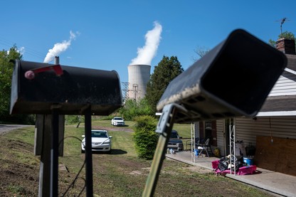 Two black mailboxes in the foreground partially obscure stacks of an industrial facility billowing white steam in the background