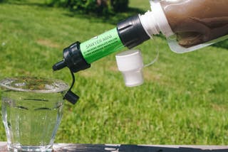 Our personal water filter pick, attached to a muddy brown bottle of water, trickling clear water into a cup