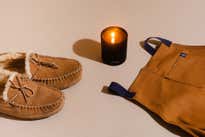 L.L.Bean Wicked Moccasins, a lit Apothke candle, and an apron are displayed on a plain background from our list of picks.