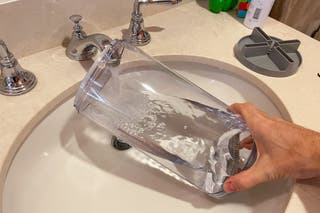 A closeup of the tank of a humidifier being filled with water in a bathroom sink as a hand holds it up.