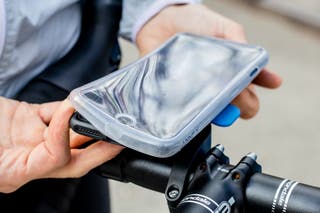 A person slips the clear Quad Lock rain cover onto a smartphone attached with a bike phone mount to a set of handlebars.