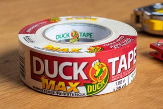 A roll of Duck Brand MAX Strength Duct Tape on a wooden workstation.