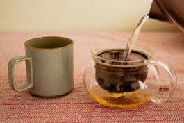 A Hasami Porcelain Mug next to a Hario Chacha Kyusu ‘Maru’ Teapot with tea being poured into it.