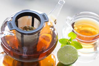 The Finum Brewing Basket inside a glass pot, in the process of brewing. A cup of the same tea from the pot sits nearby.