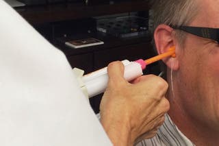 A person receiving foam ear impressions from an audiologist.