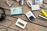 Cassette players, tapes and a pair of headphones scattered on a wood table.