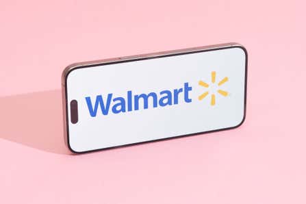 The Walmart logo on a smartphone lying horizontally on a pink background.