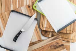 About a dozen different cutting boards stacked on top of one another with a chopping knife sitting on top of the pile.