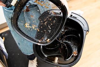 An air fryer that has been opened to reveal a greasy basket and a pool of grease collected at the bottom.