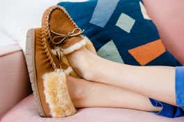 Person sitting on a pink velvet couch, wearing the L.L.Bean Wicked Good Moccasins.