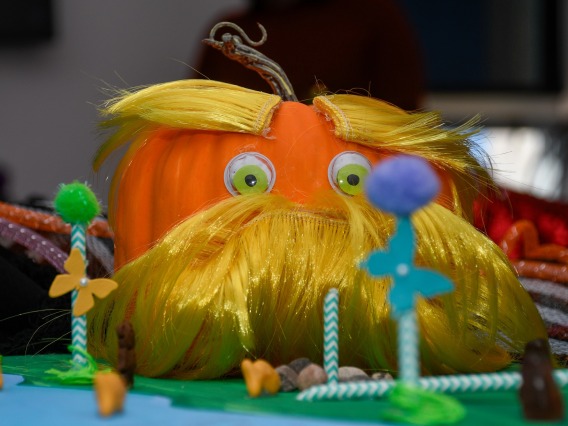 A pumpkin with fake eyes and a yellow mustache and eyebrows attached to it.