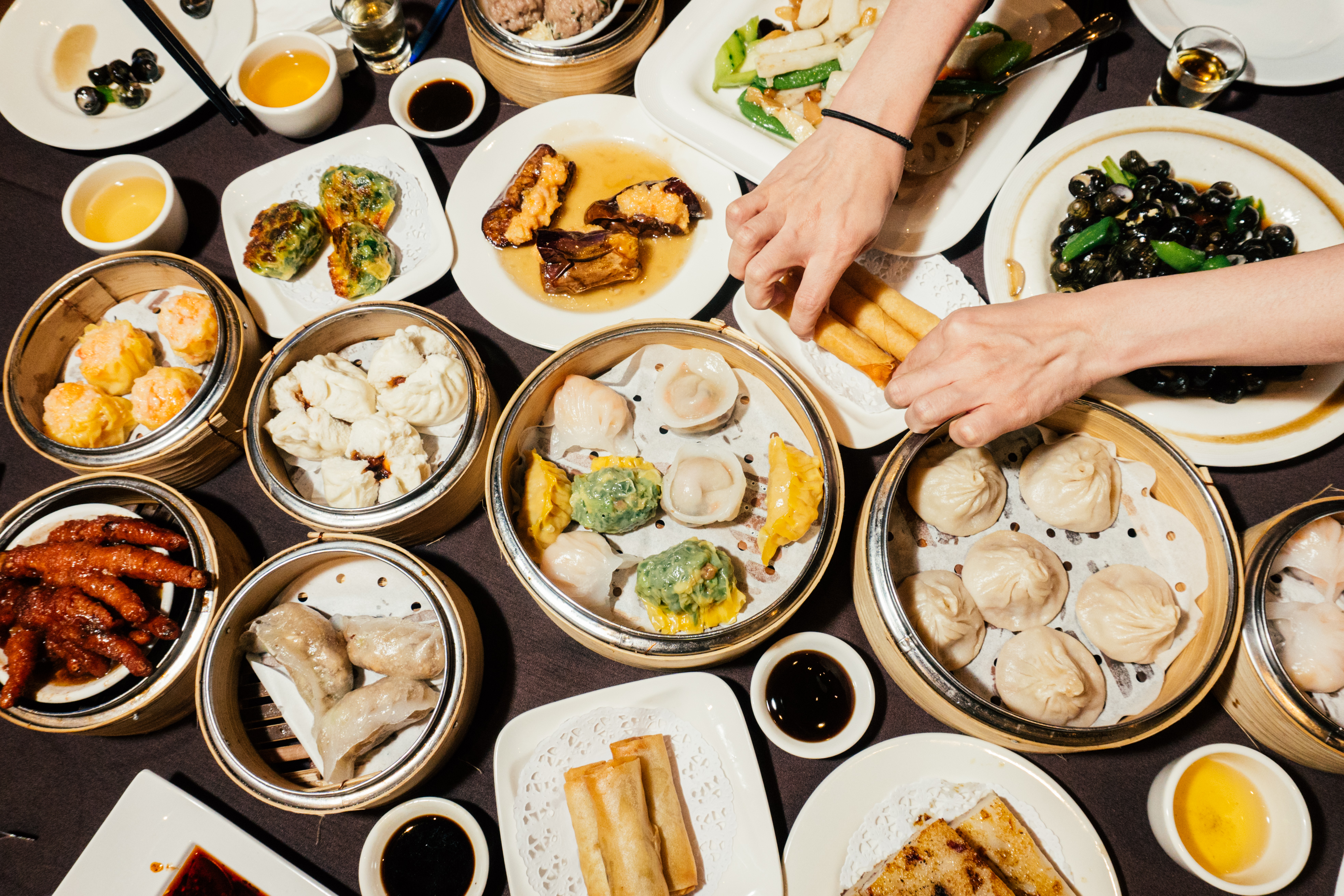 A table is crowded with various dim sum, including chicken feet, stuffed eggplant, and spring rolls.