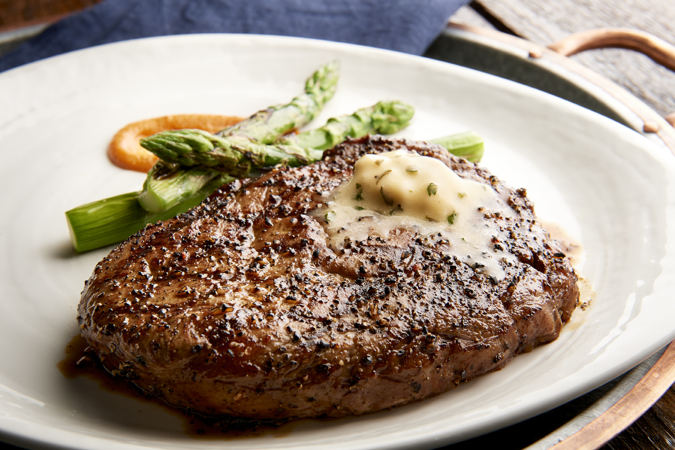 A steak from Jake’s Grill on a white plate with butter on top