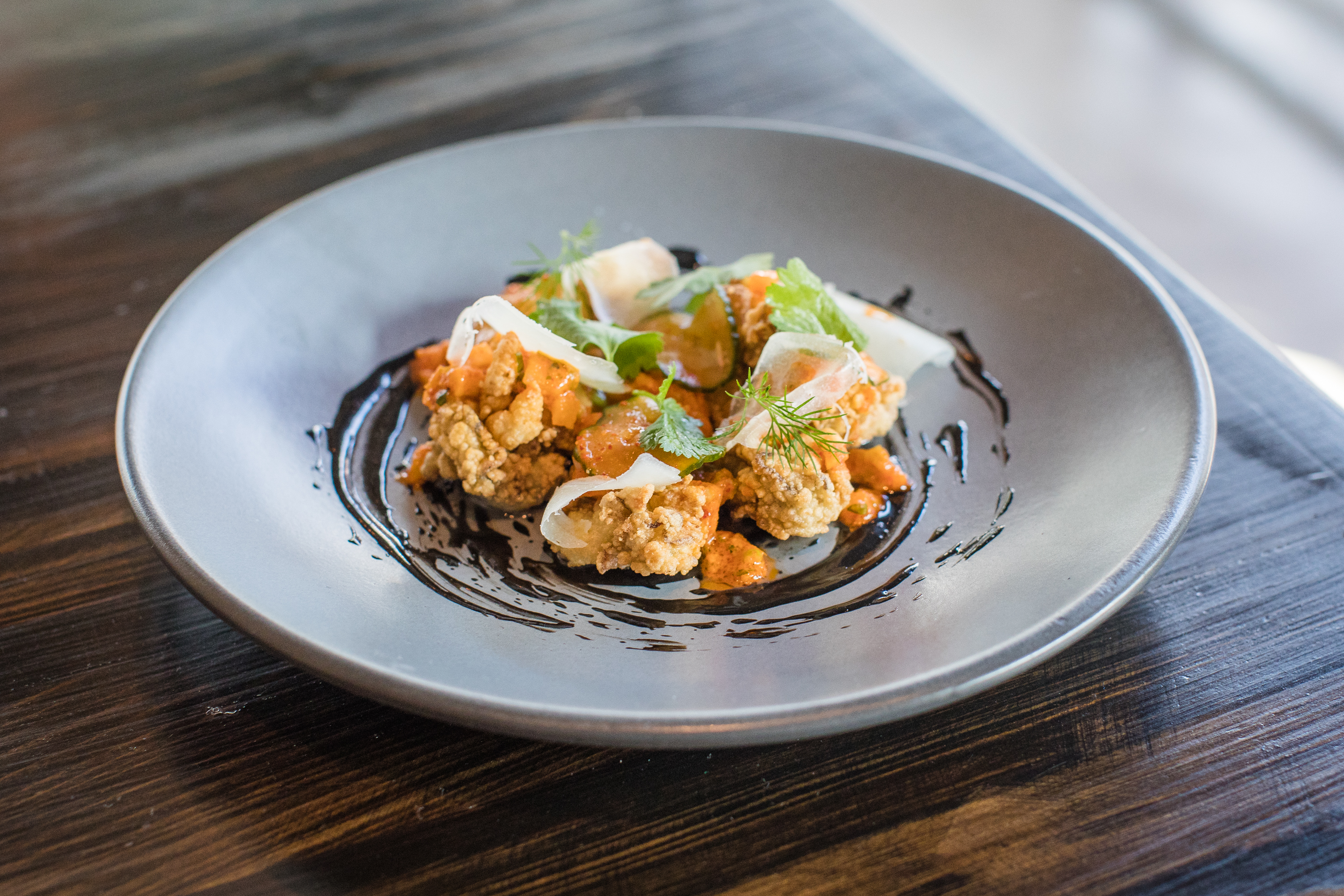 A plate of delicate fried oysters topped with orangey red sauce and cilantro. 