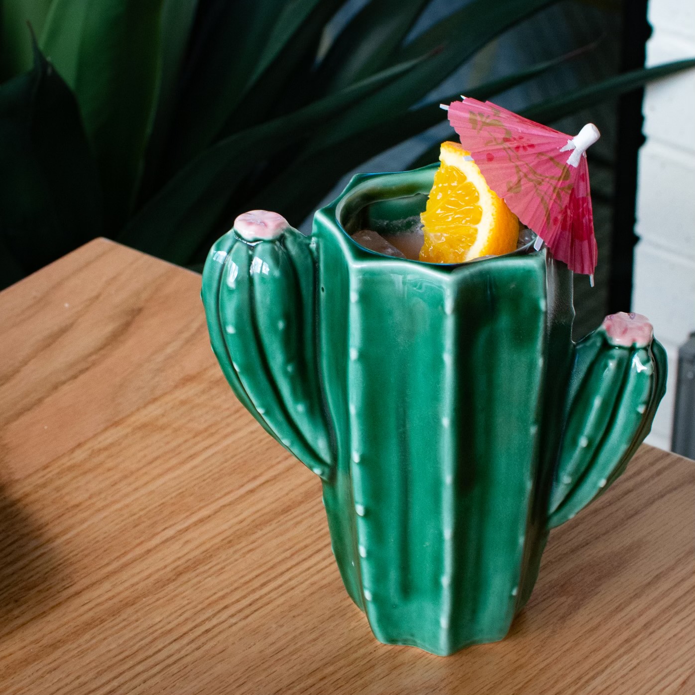 View of a wooden table counter with a green cactus-shaped cocktail glass in the foreground.