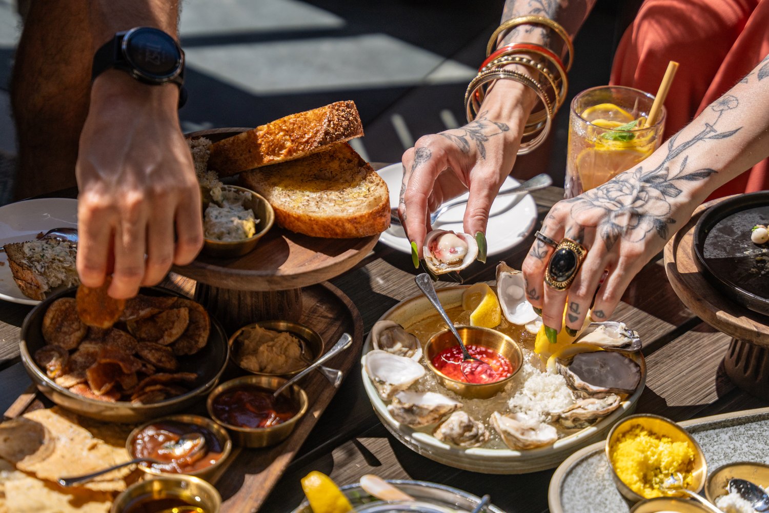 Diners dig into trays of oysters and dips in a sunny spot.