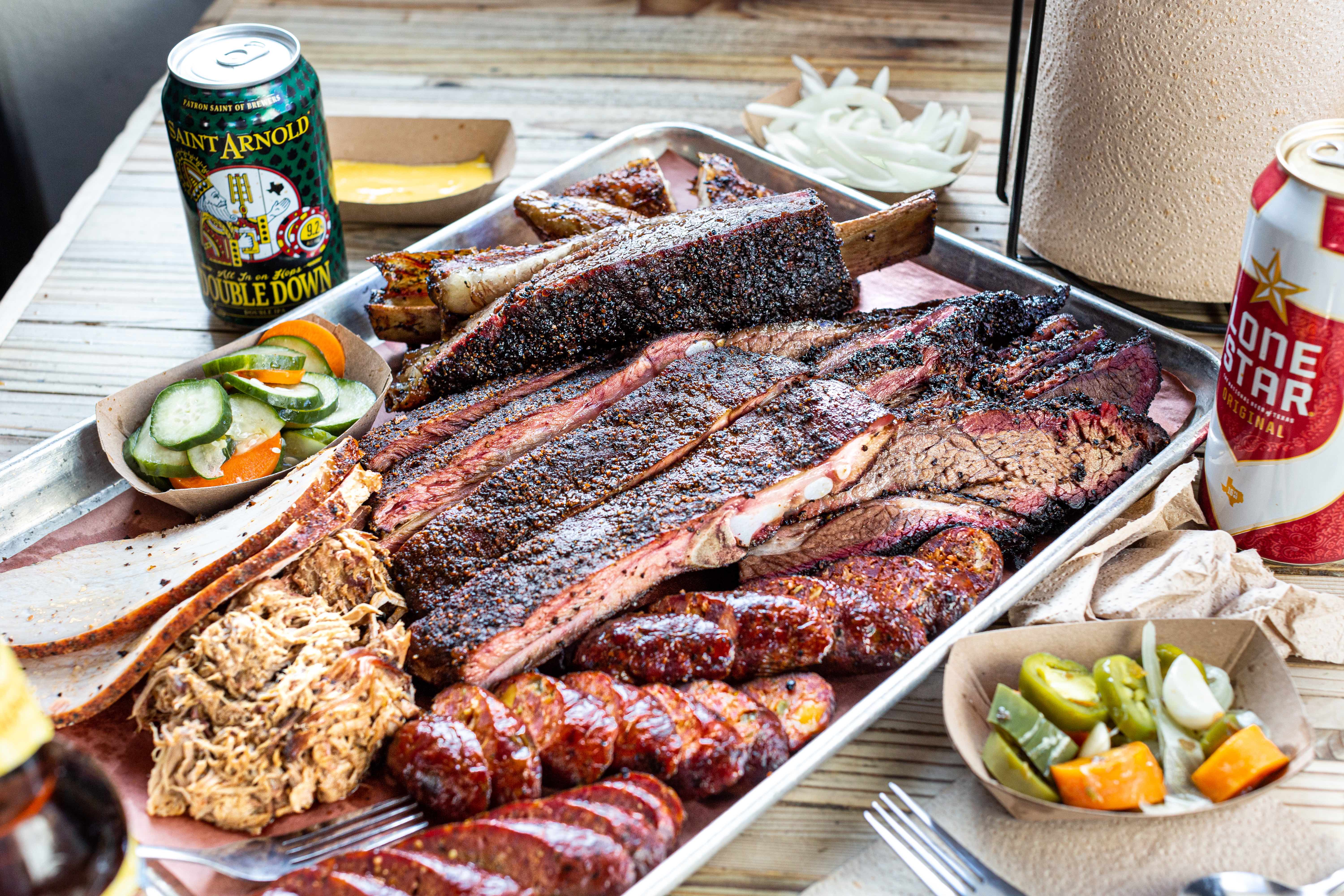 A metal tray of the Pit Room’s ribs, pulled pork, pickles, brisket, sausage, with a can of Saint Arnold’s Double Down beer.