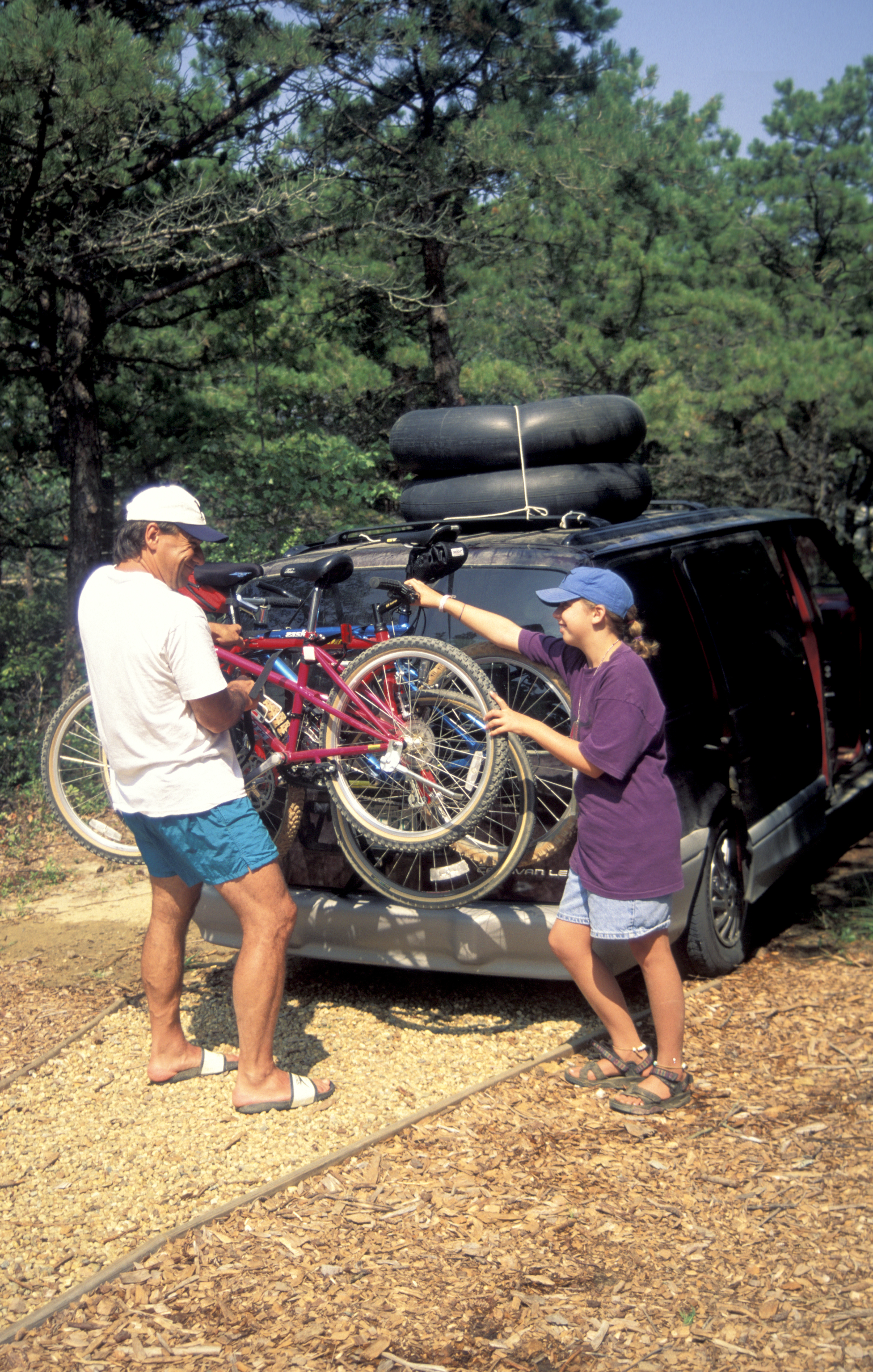 Father And Daughter Loading Minivan With Bikes And Inner Tubes.