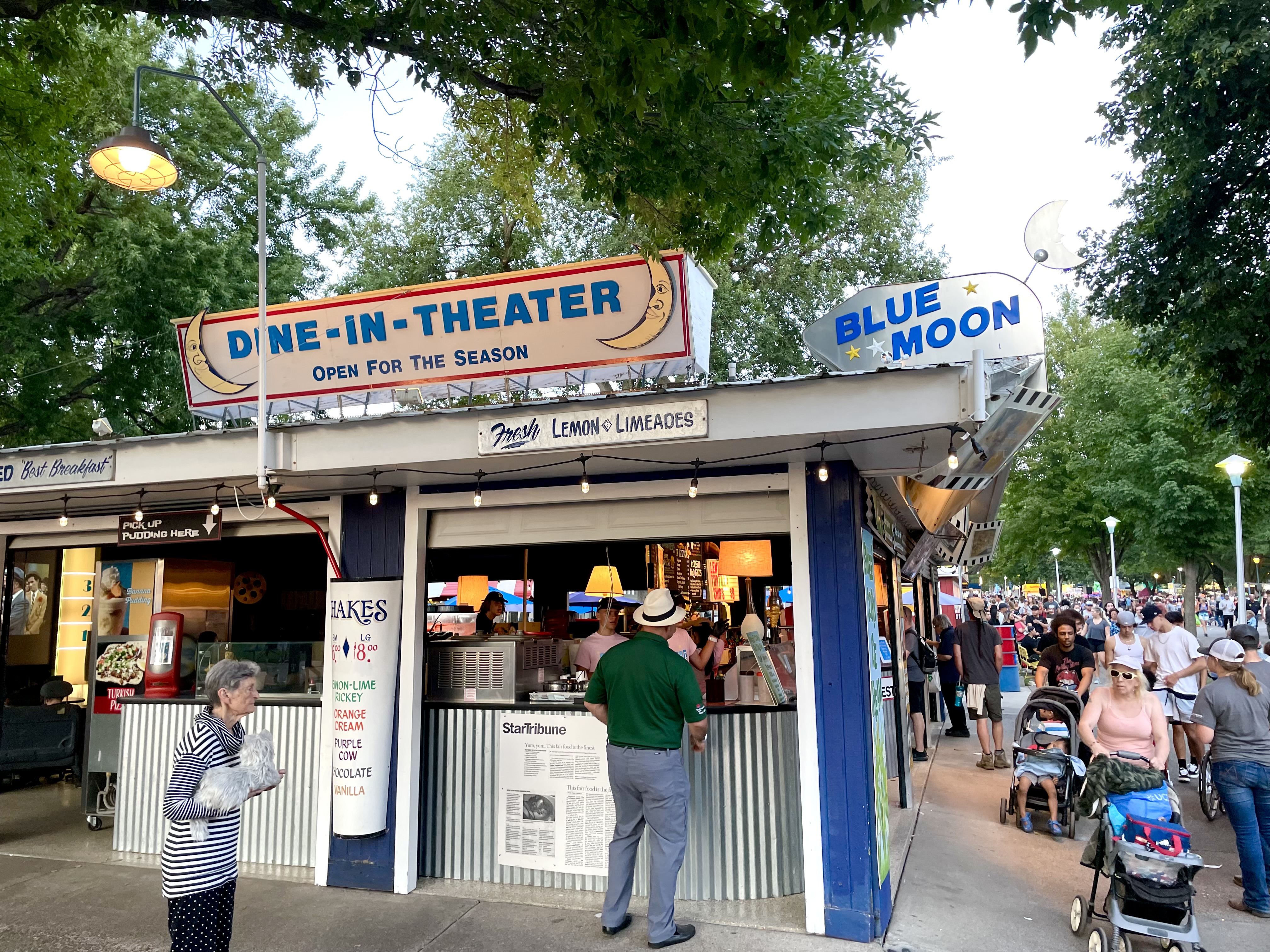 The exterior of a blue-painted building that reads “Dine-In-Theater” with people milling around it. 