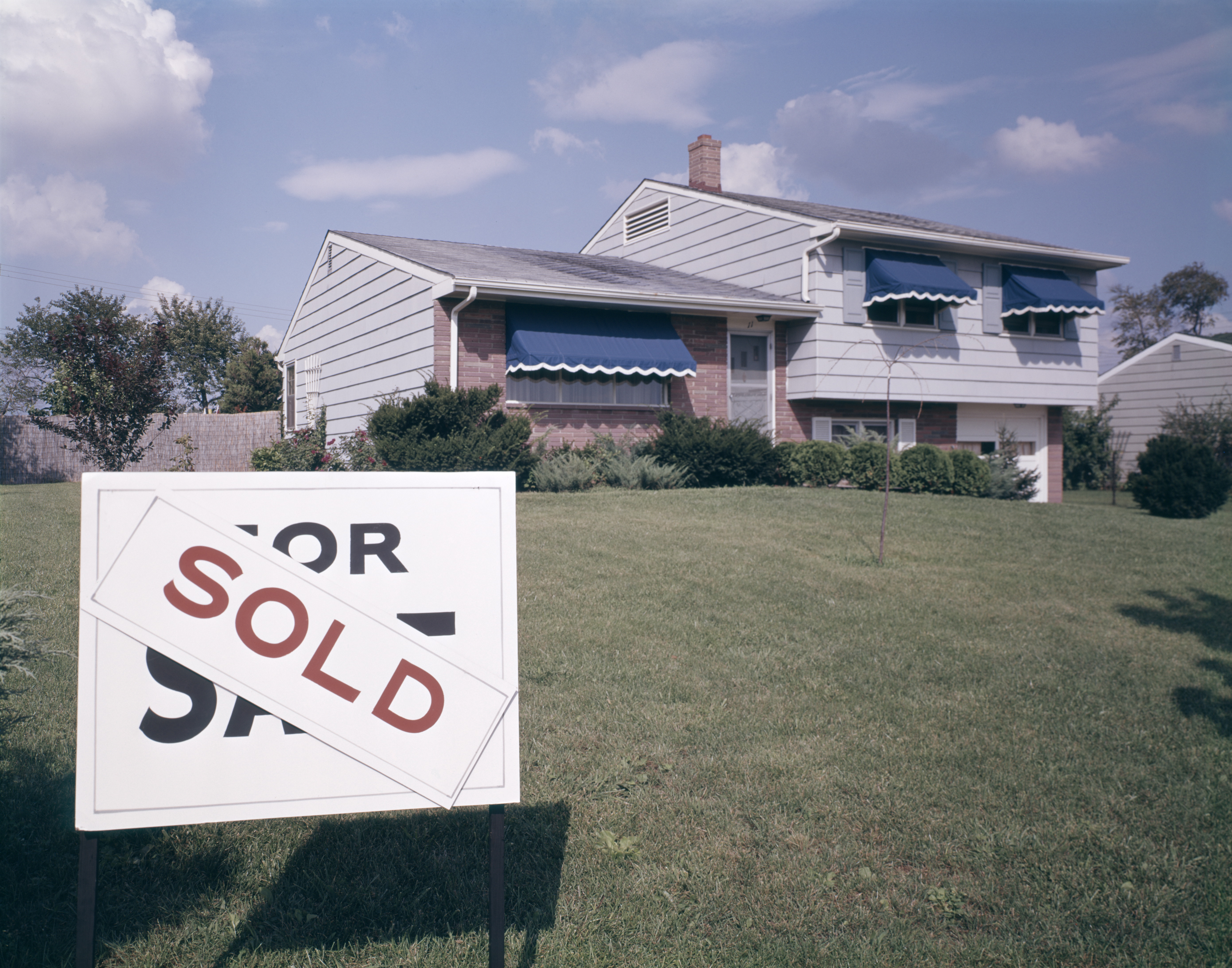 Suburban House With Blue Awnings And A Sold Sign O