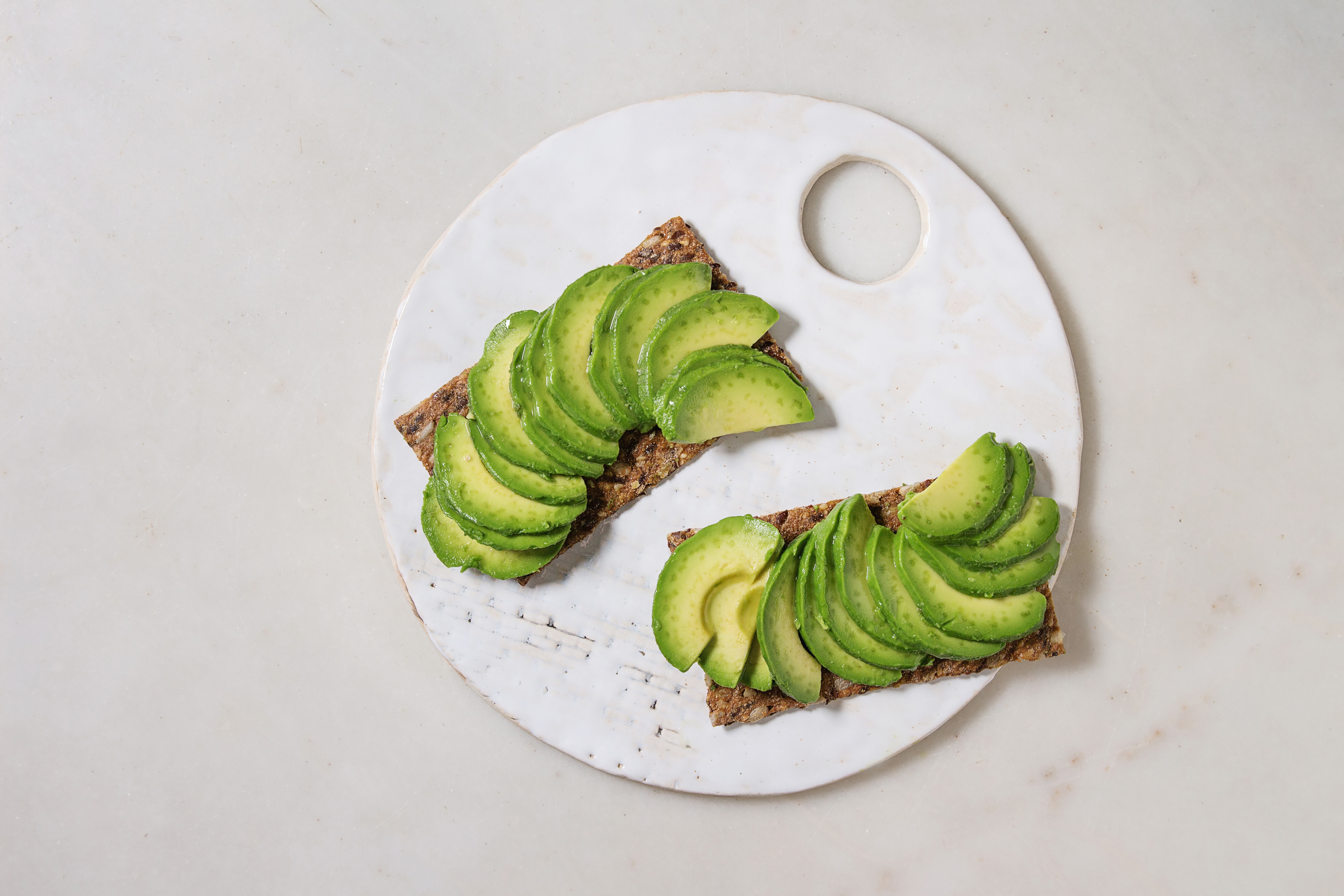 Vegan sandwiches with sliced avocado on rye bread served on ceramic board over white marble background. Flat lay. space.