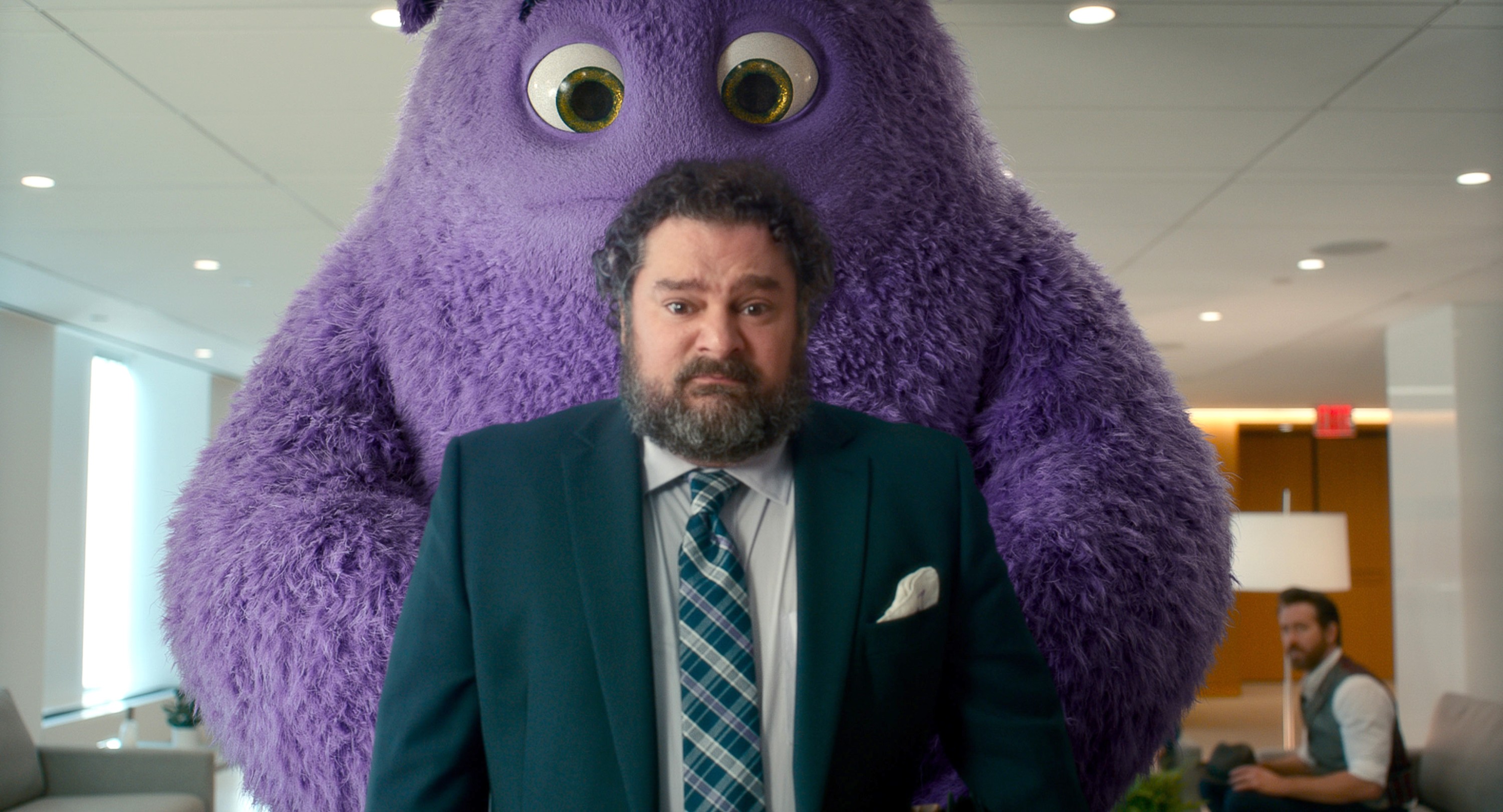 A huge purple furry imaginary friend stands behind a suited, bearded businessman (Bobby Moynihan) who’s making a sour face in John Krasinski’s IF