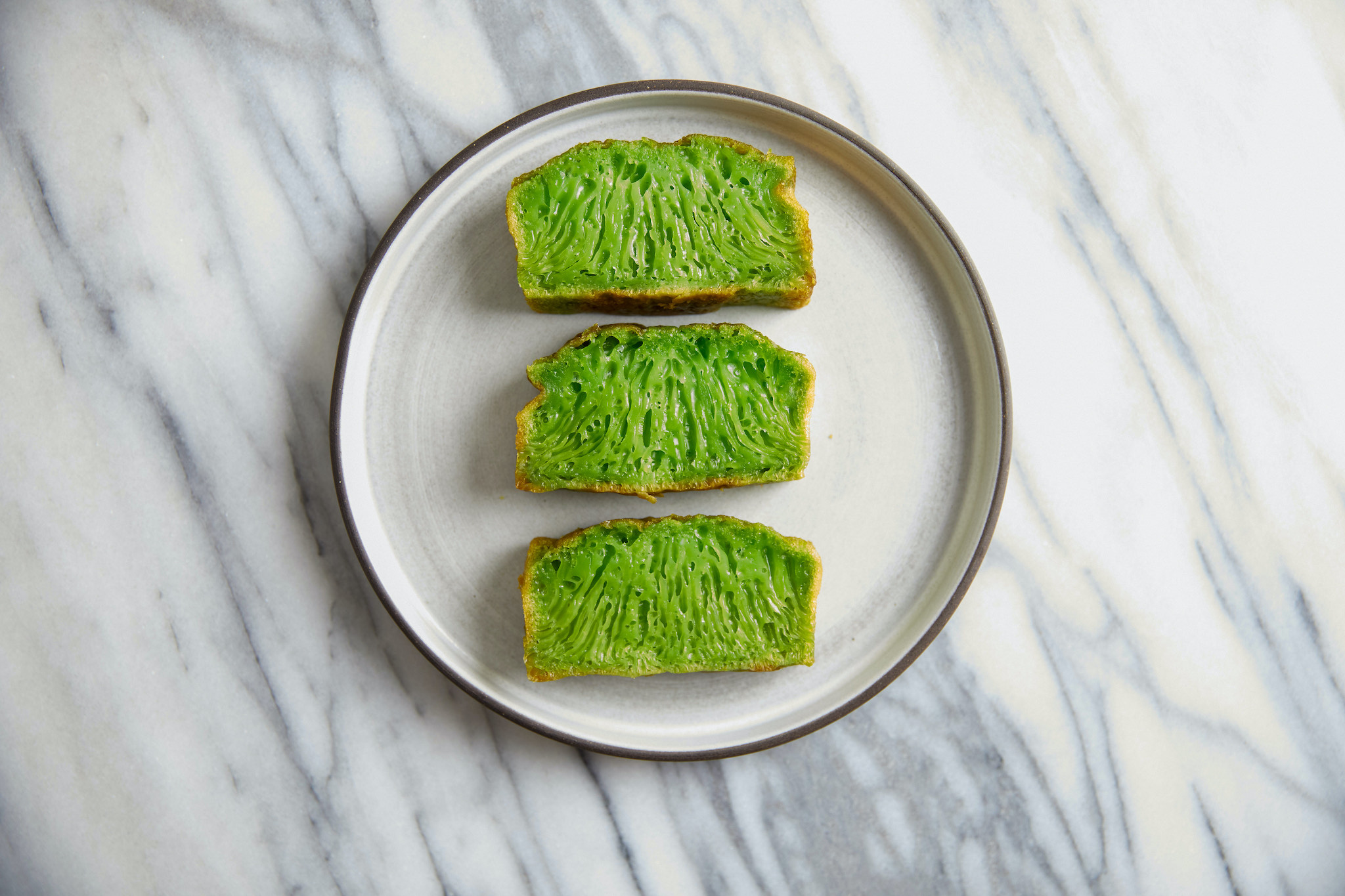 Three slices of bright green banh bo, a Vietnamese dessert, on a ceramic plate.