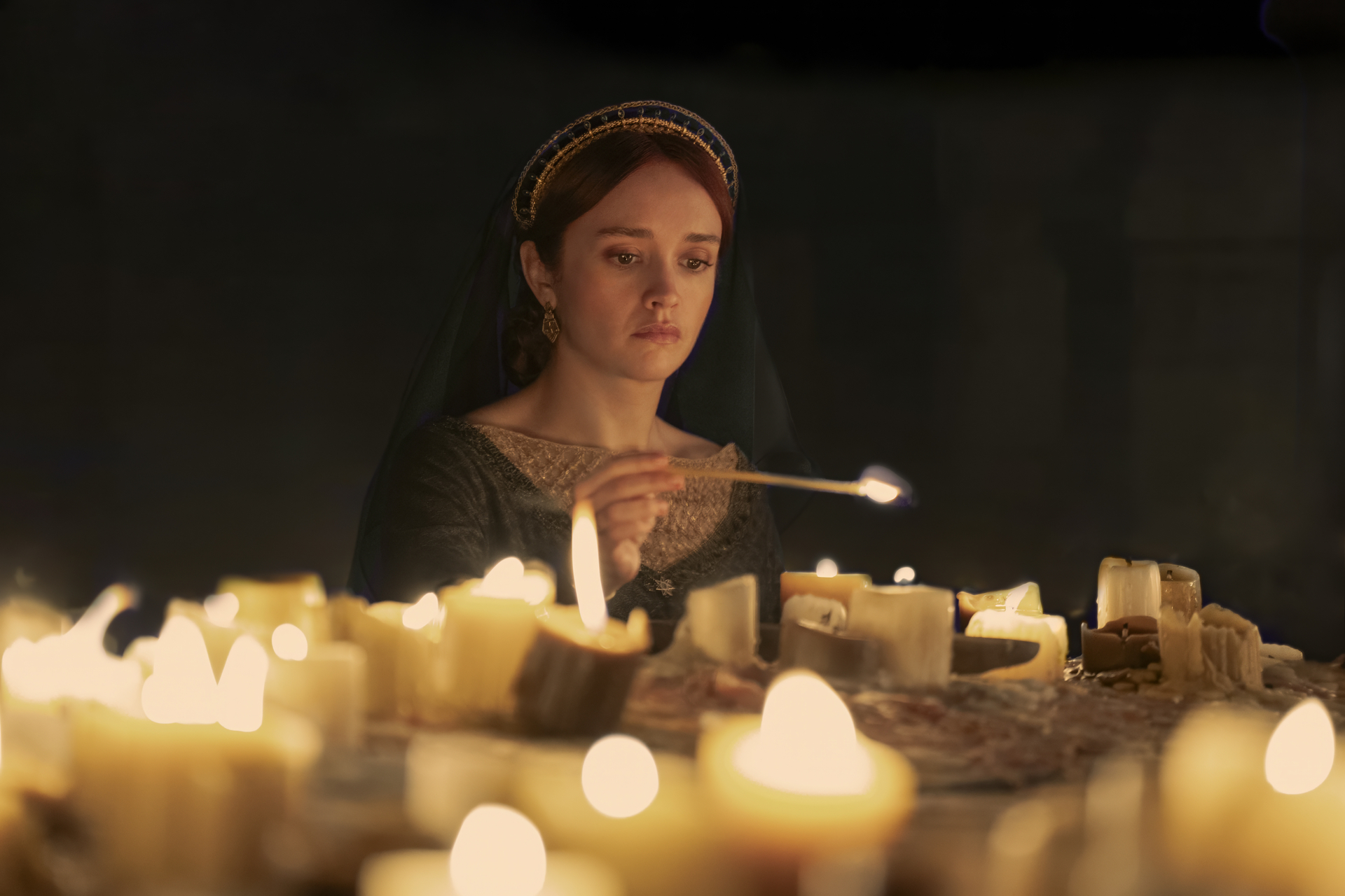 Alicent lights a bevy of candles in a dark room in House of the Dragon season 2