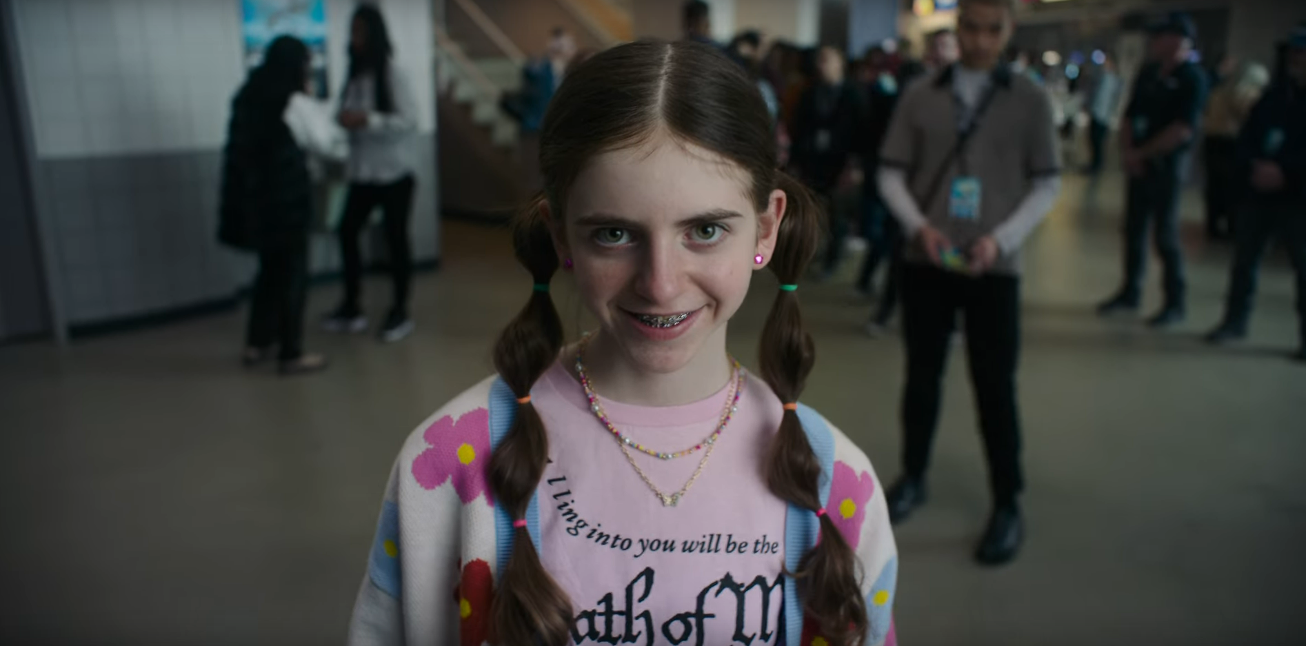 A little girl looks toward the camera while walking toward it with an unnatural grin on her face in Smile 2 