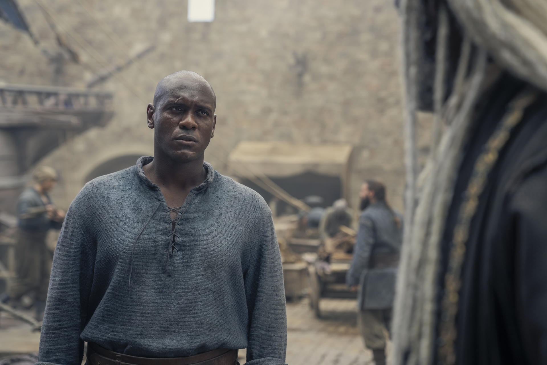 Abubakar Salim as Addam of Hull in House of the Dragon season 2, standing on a dock looking toward Steve Toussaint as Colys Velaryon